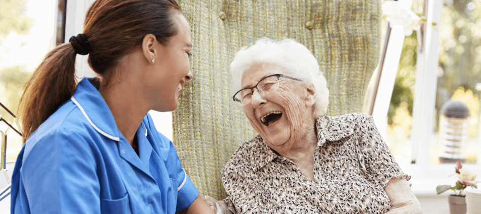 Elderly woman laughing joyously while a health assistant smiles back
